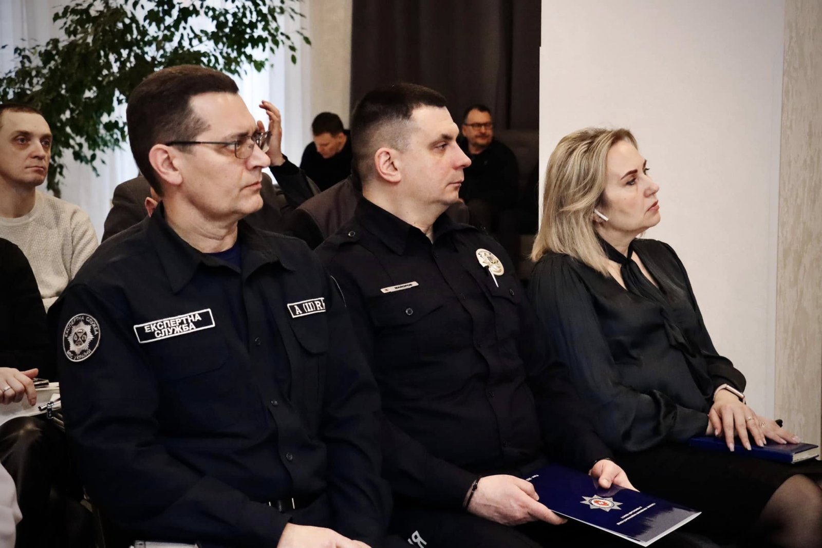 Двоє чоловіків та жінка присутні на діалоговій зустрічі та слухають доповіді.