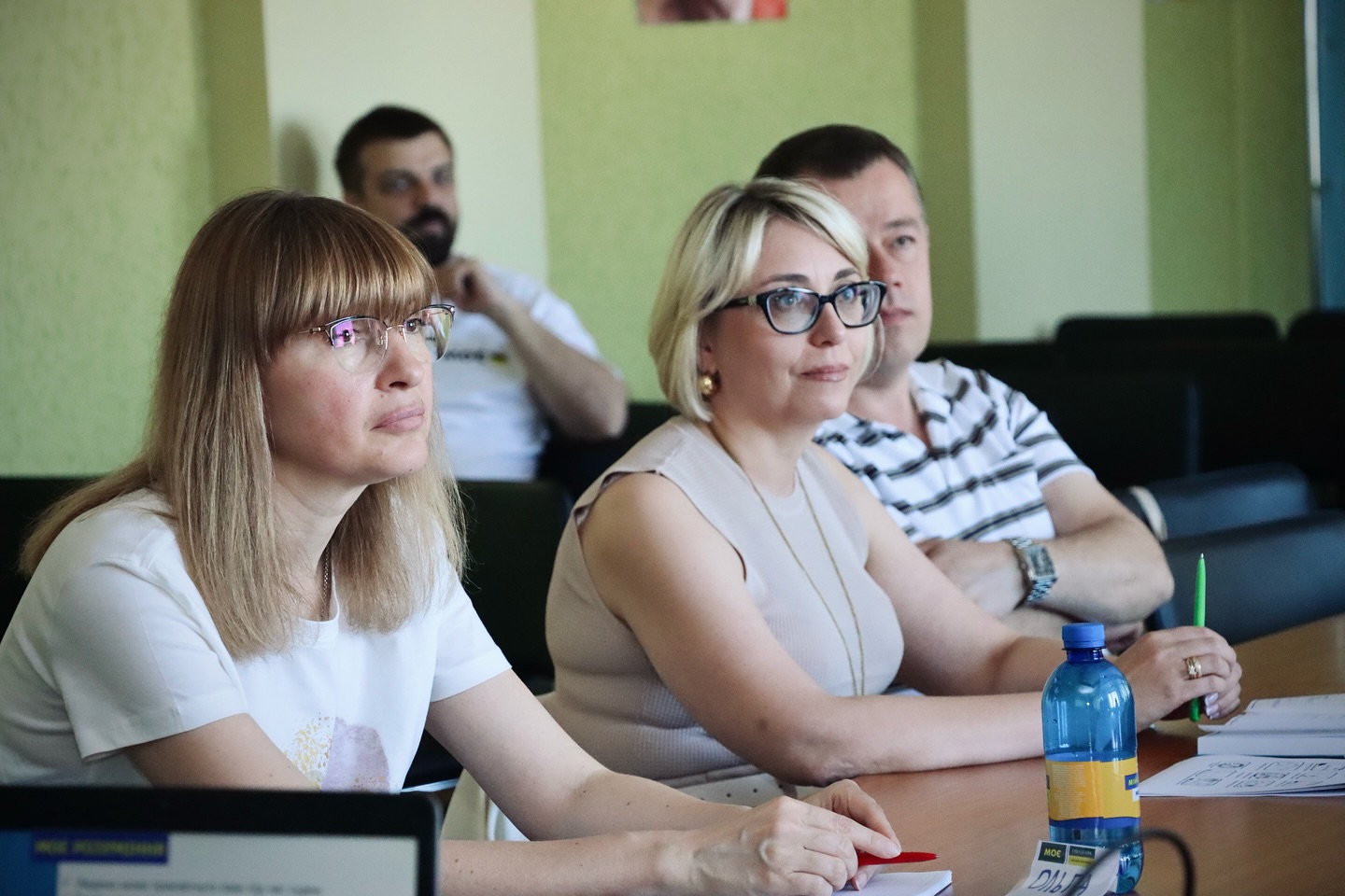 Група людей — дві жінки на передньому плані та двоє чоловіків позаду — уважно слухають.