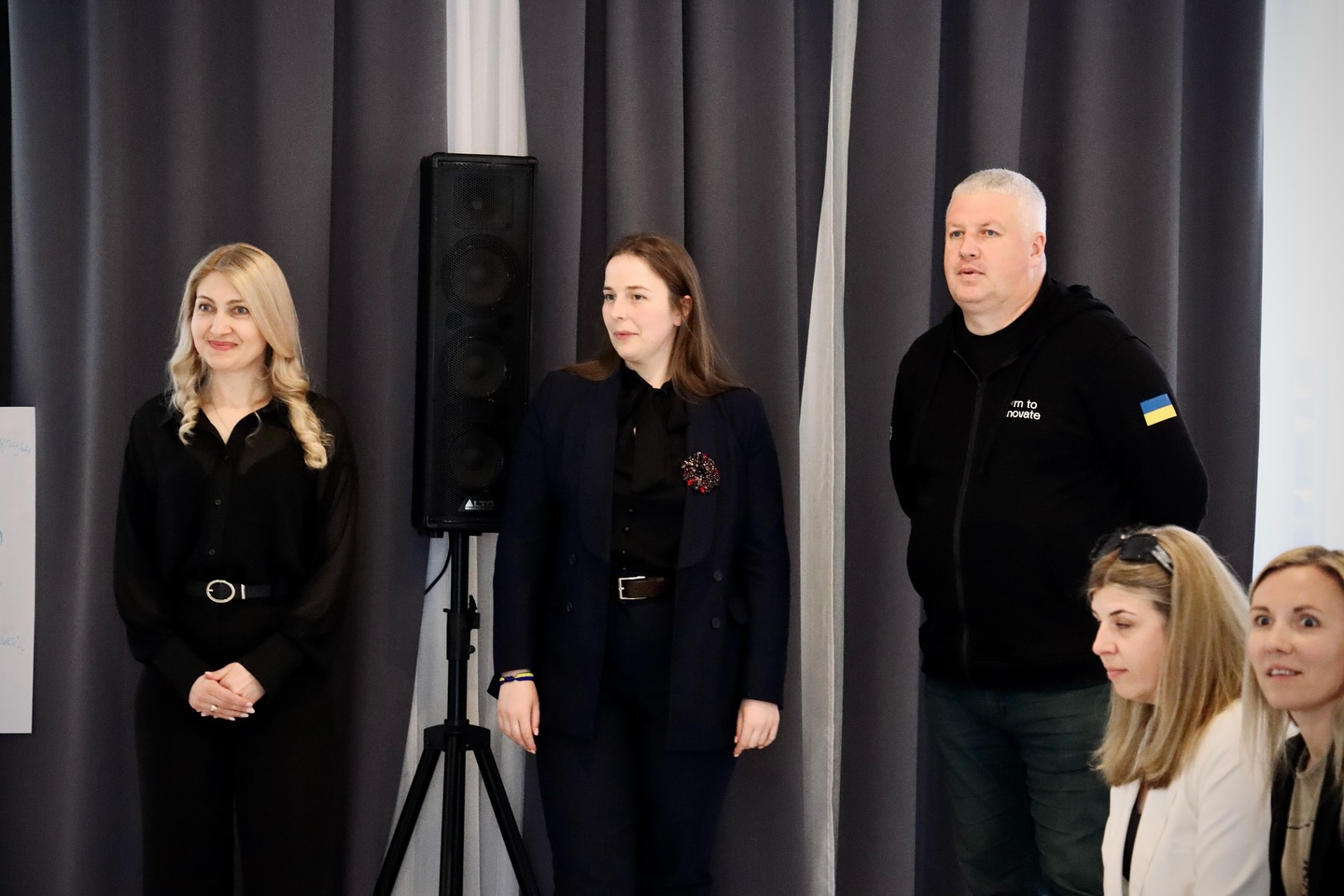 Дві жінки та чоловік стоять у приміщенні.