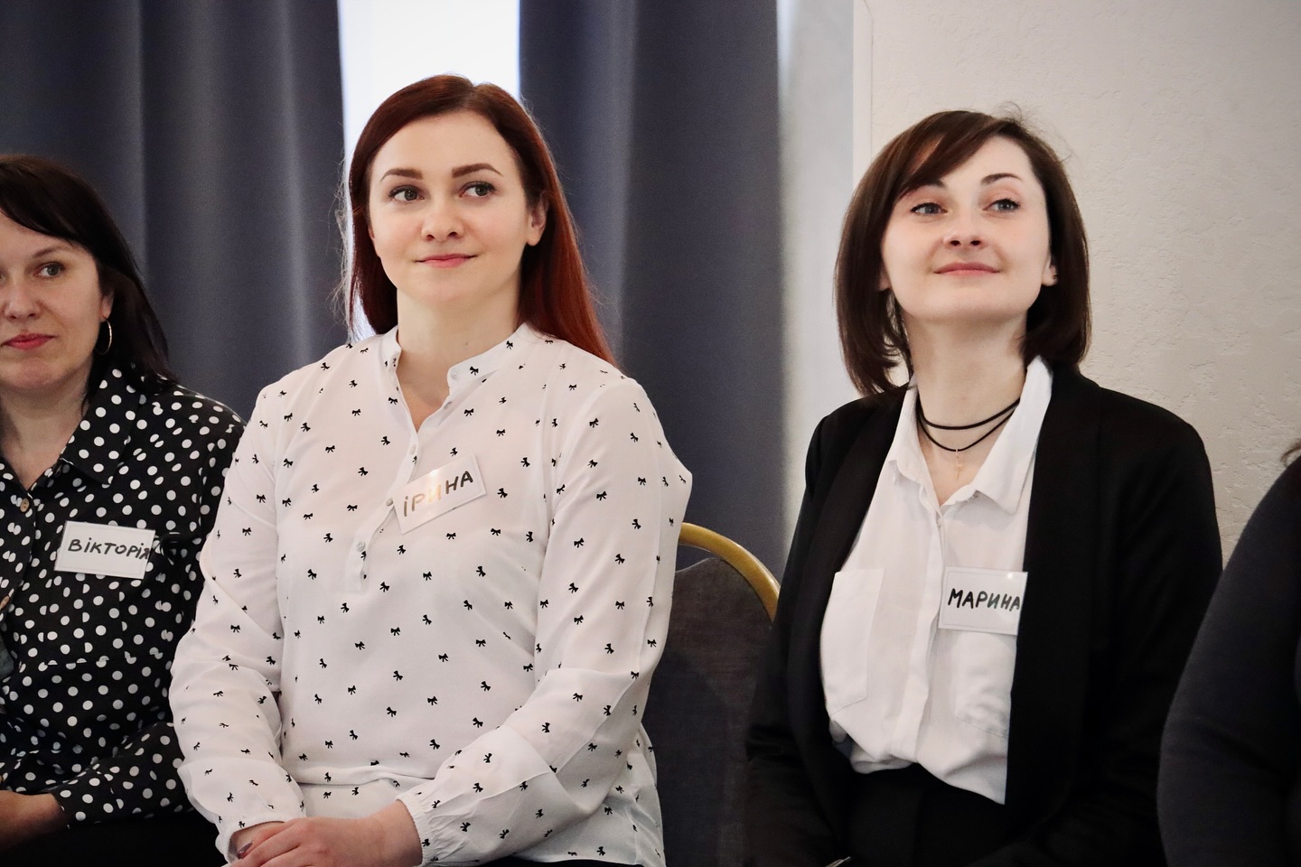 Дві жінки у діловому одязі сидять у приміщенні.