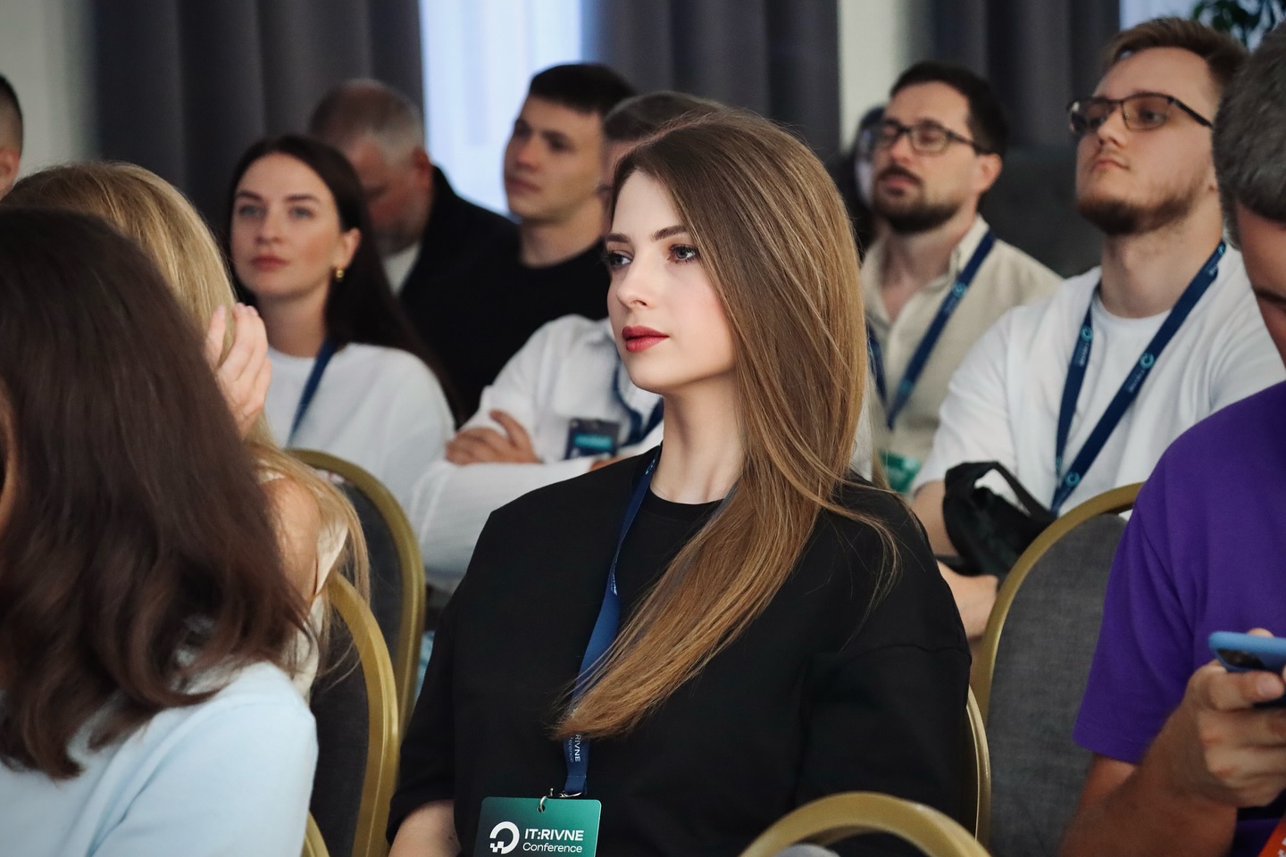 Люди сидять у залі, на передньому плані жінка з бейджем.