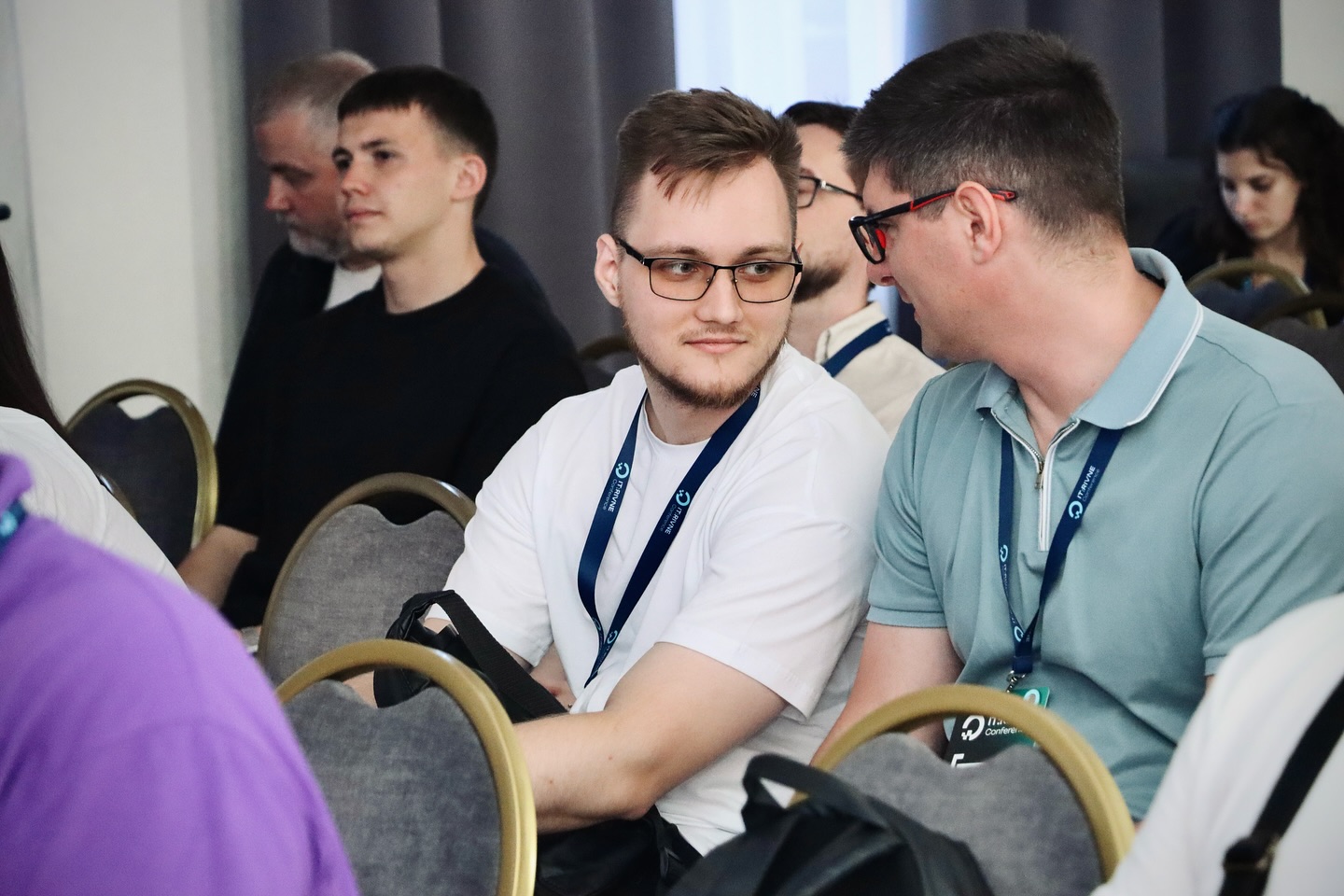 Двоє чоловіків у залі конференції ведуть розмову, навколо інші учасники.