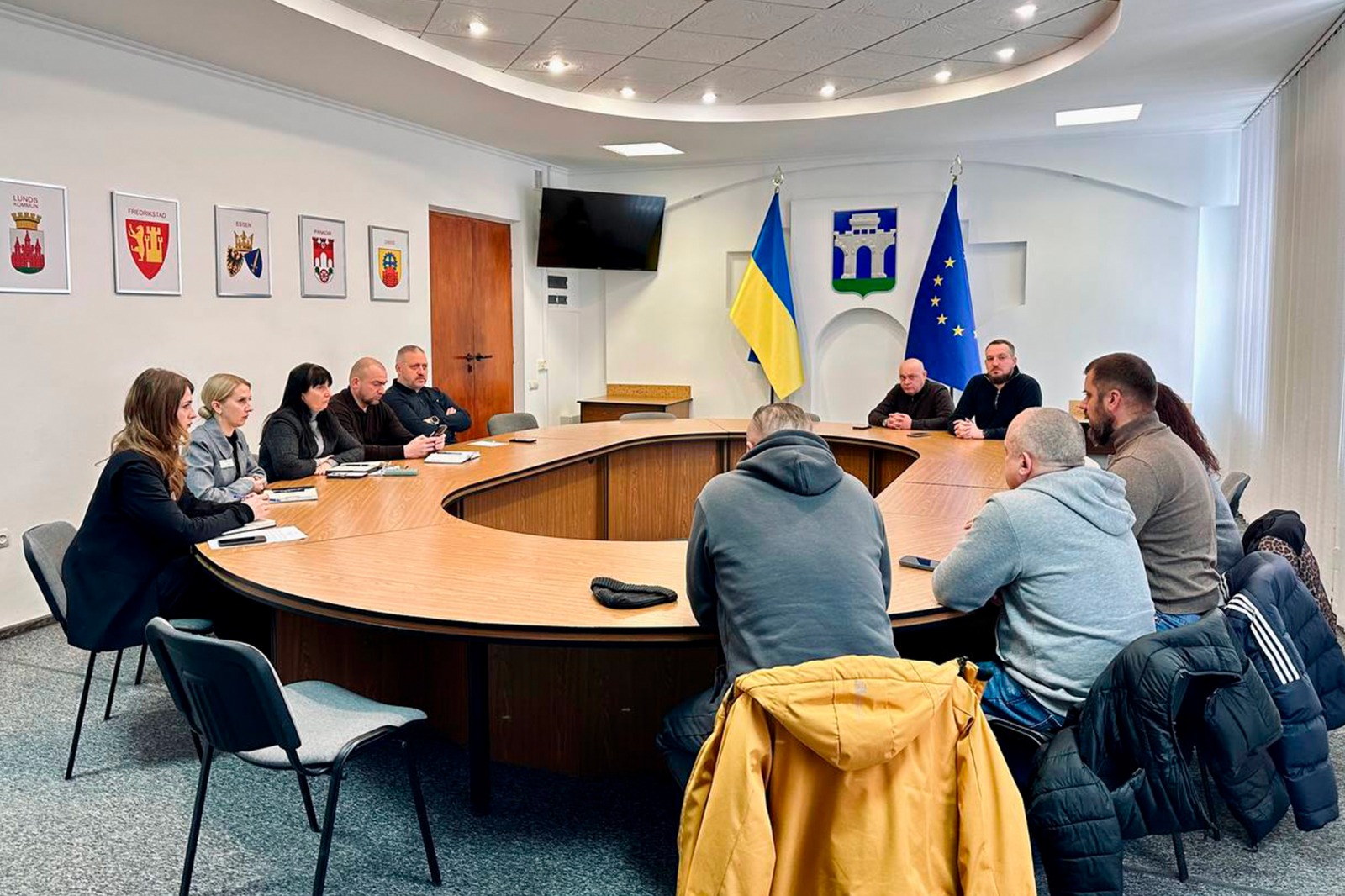 Група людей сидять за круглим столом, у приміщенні.