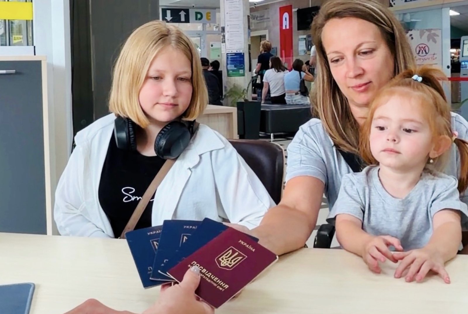 Жінка з двома дітьми сидить у приміщенні.