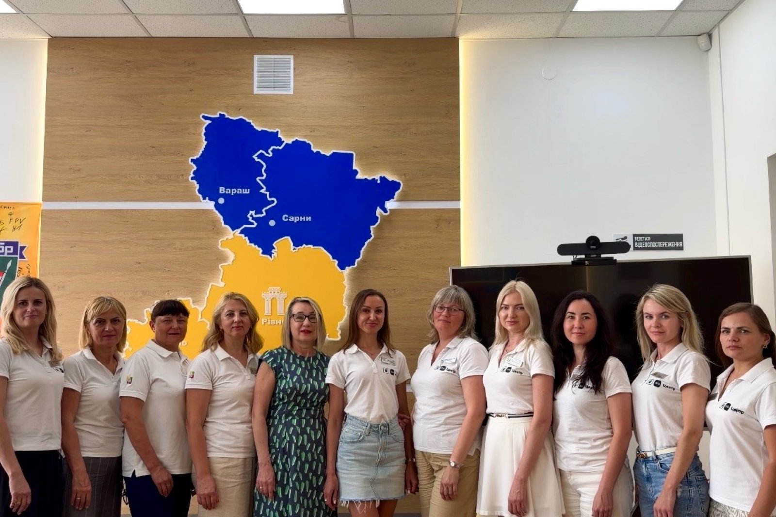 Група жінок позують для спільного фото на фоні карти Рівненської області у синьому та жовтому кольорах.