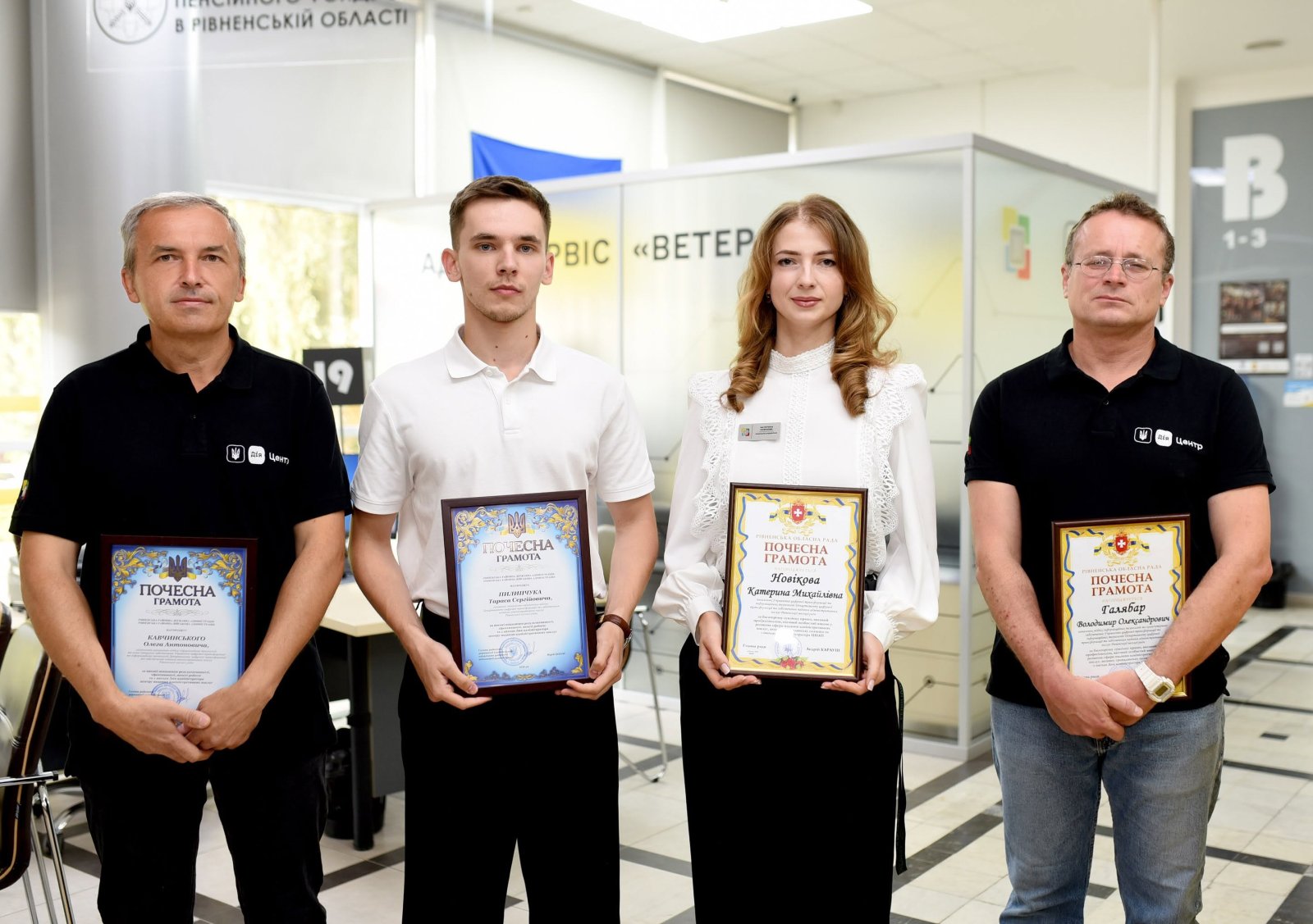 Жінка та троє чоловіків позують з грамотами.