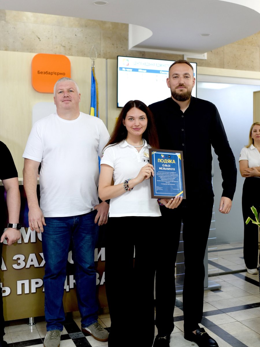 Жінка позує з грамотою, біля неї стоять двоє чоловіків.