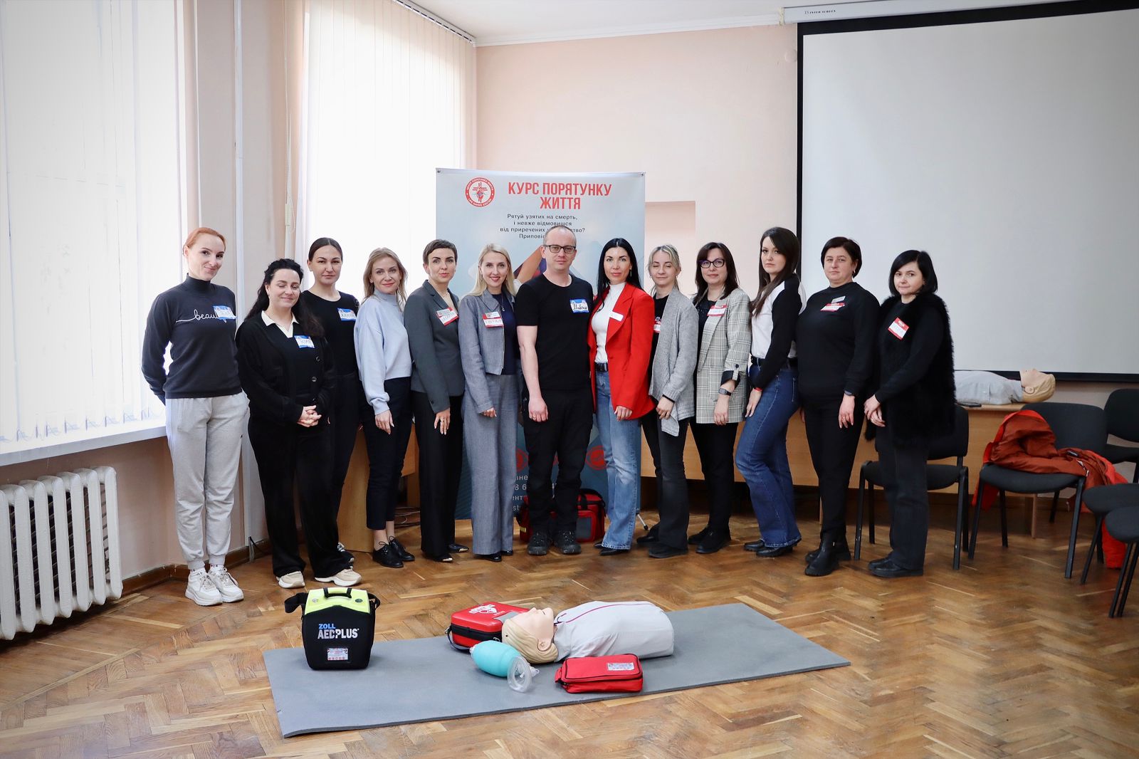 Групове фото в приміщенні, на передньому плані лежить манекен