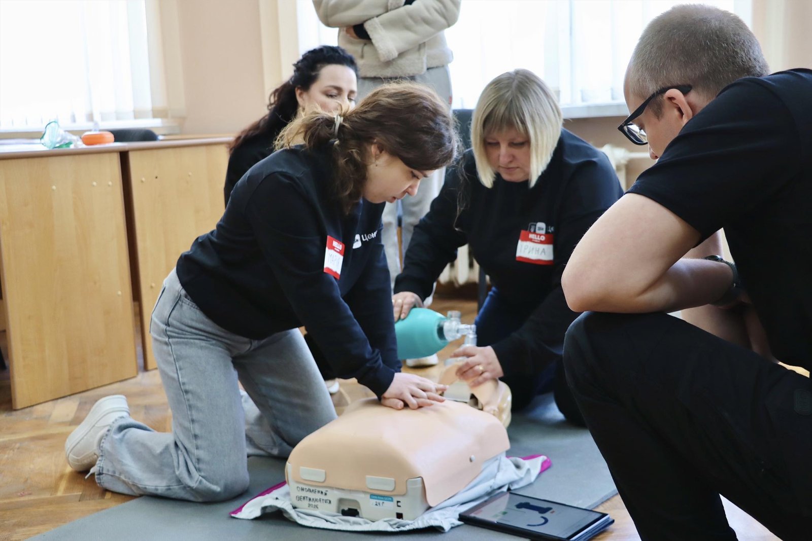 Дівчина робить непрямий масаж серця на манекені, жінка збоку робить вентеляцію легень.
