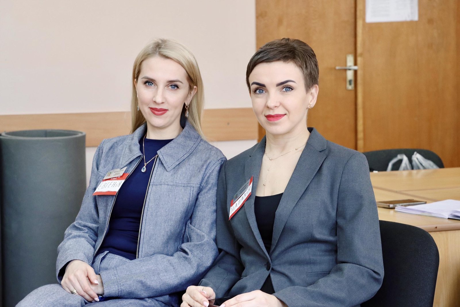 Дві жінки з бейджами посміхаються