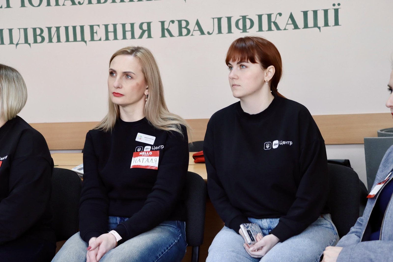 Дві жінки в темному одязі сидять у приміщенні.