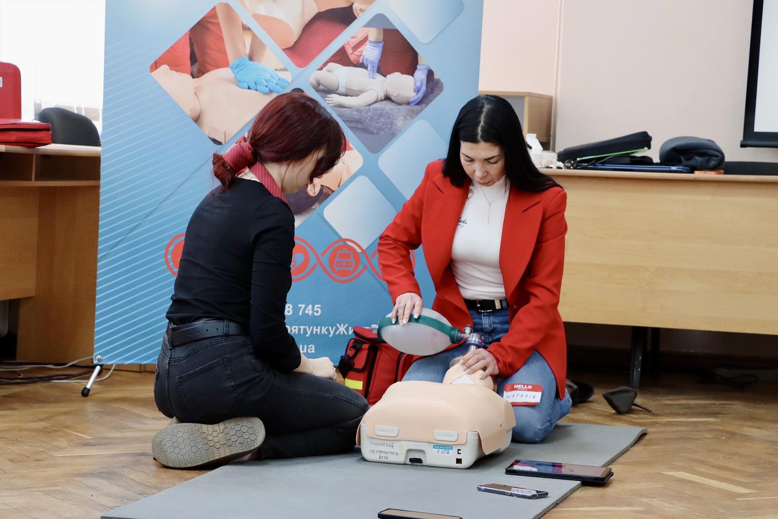 Жінка робить вентеляцію легень на манекені, інша жінка сидить збоку
