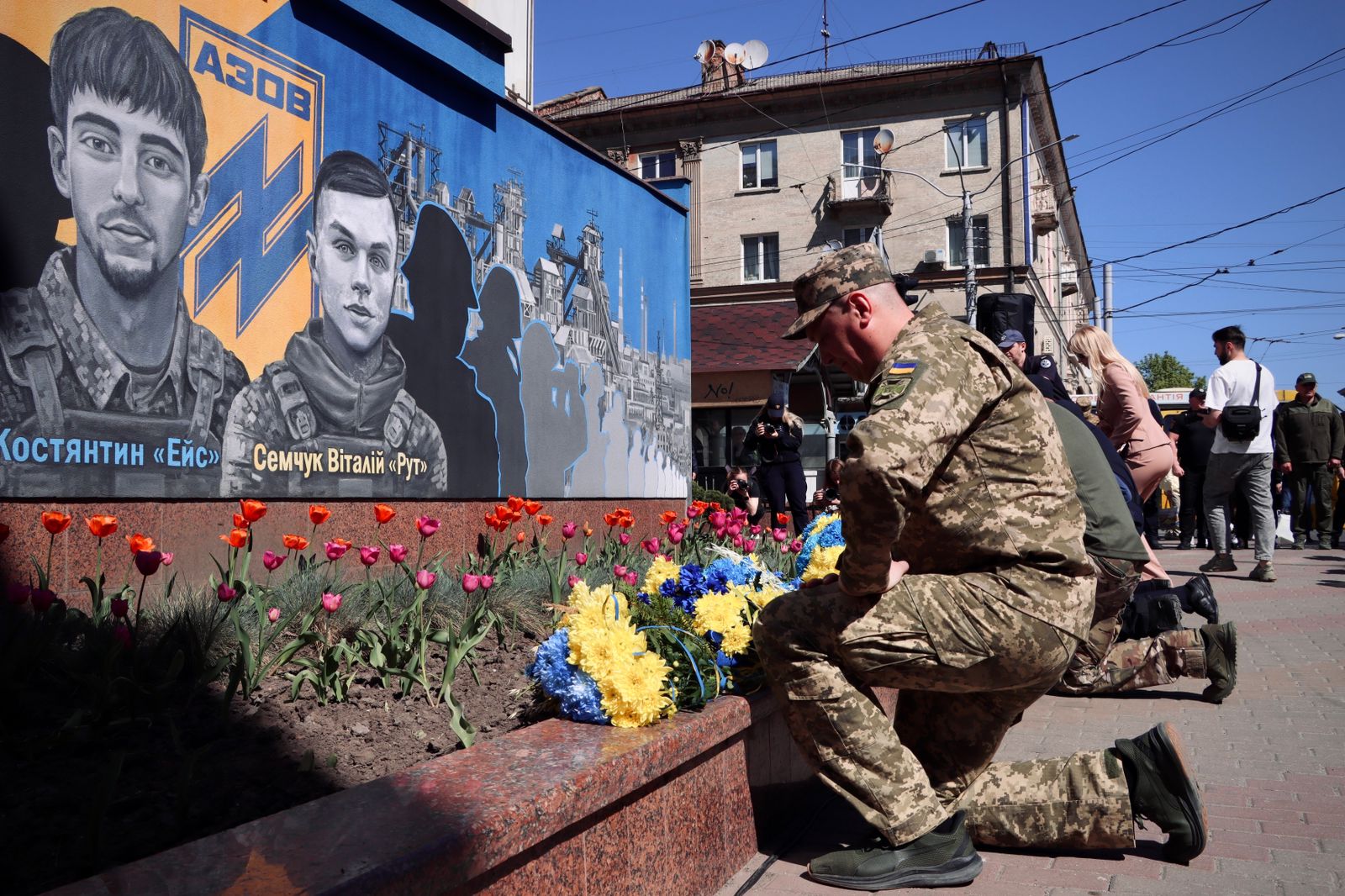 Чоловік у військовій формі стоїть на одному коліні перед муралом.