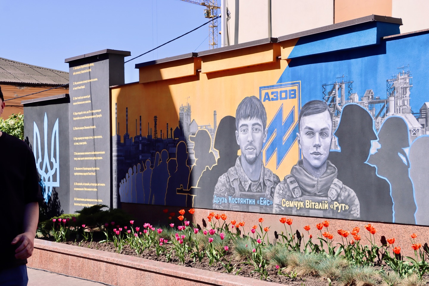 Мурал із зображенням військових і символікою Азов на стіні, перед якою висаджені тюльпани.