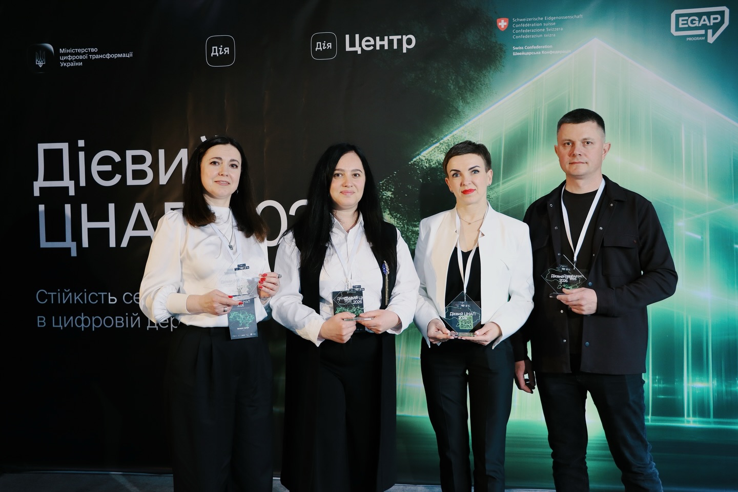 Три жінки та чоловік позують з нагородами.