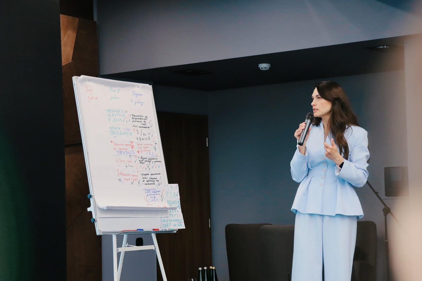 Жінка у блакитному костюмі щось розповідає у мікрофон.