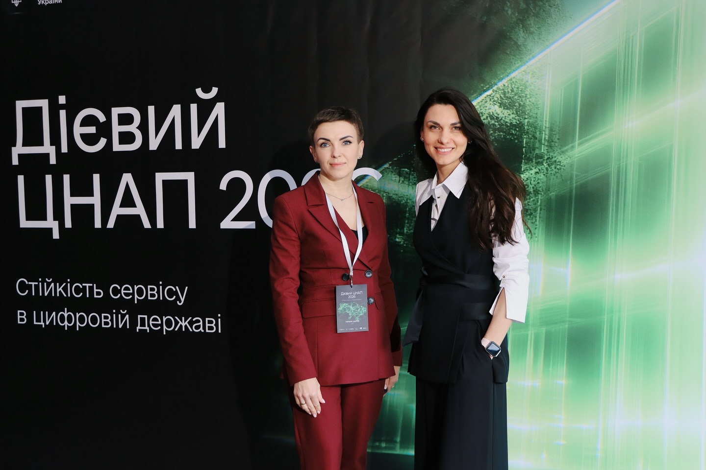 Дві жінки фотографуються на фоні банера.