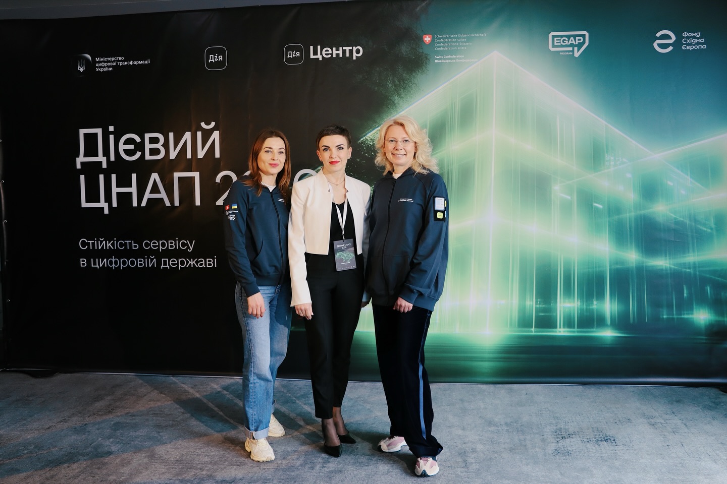 Три жінки позують на фоні банера.