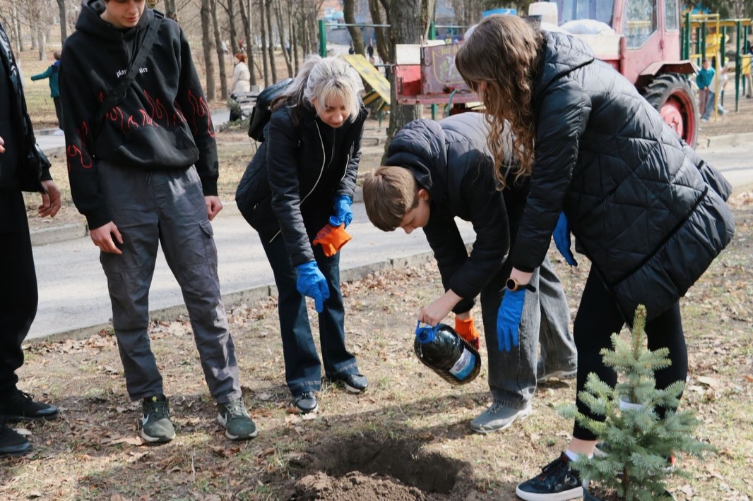 Хлопець наливає рідину у ямку, біля нього стоять дві жінки.