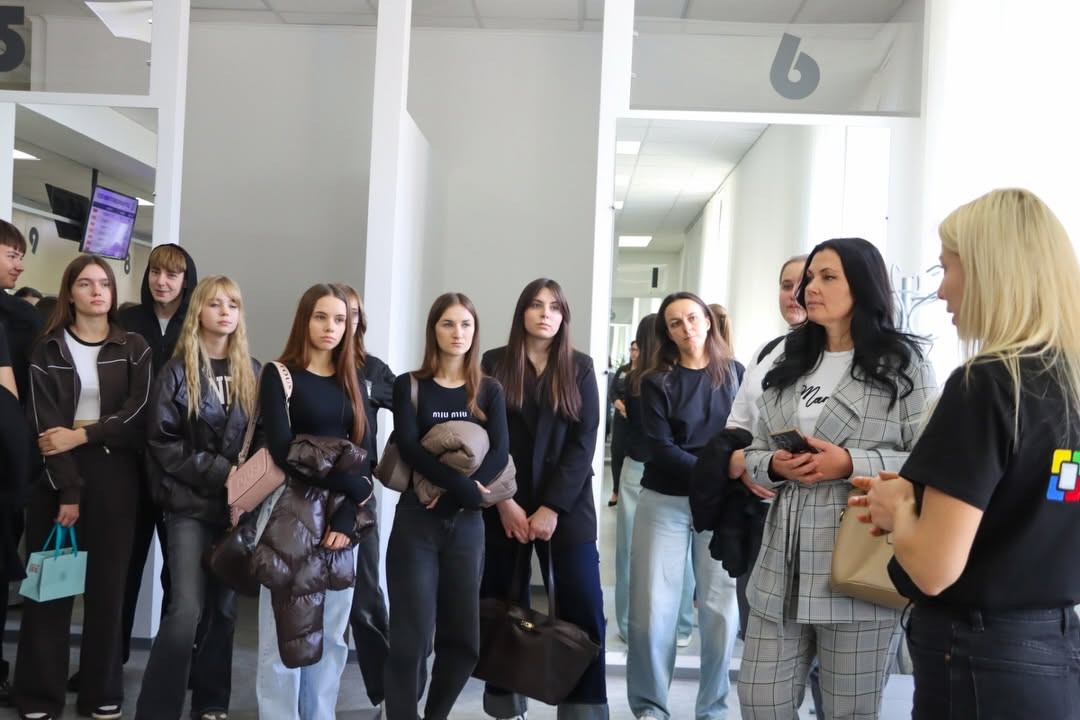 Жінка зі світлим волоссям щось розповідає для групи людей.
