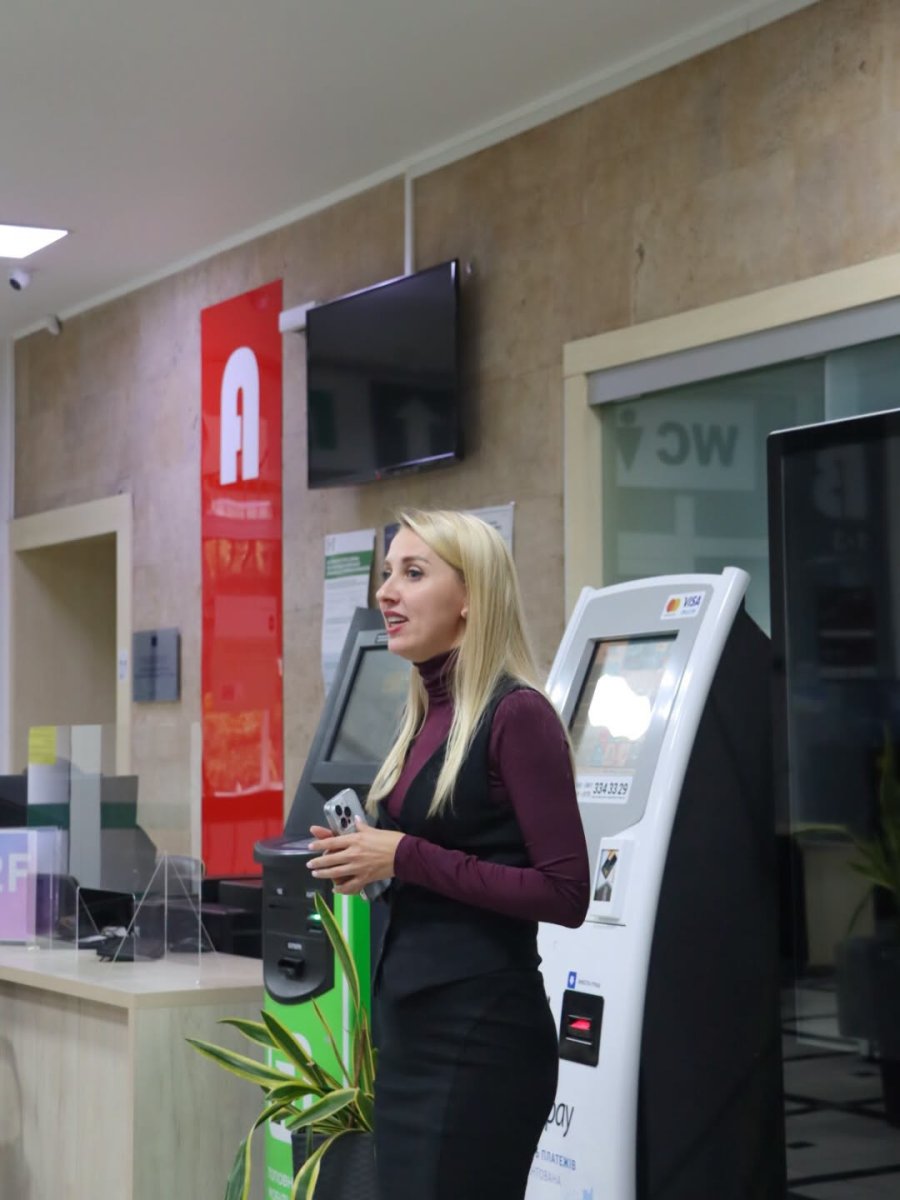 Жінка зі світлим волоссям стоїть у приміщенні.