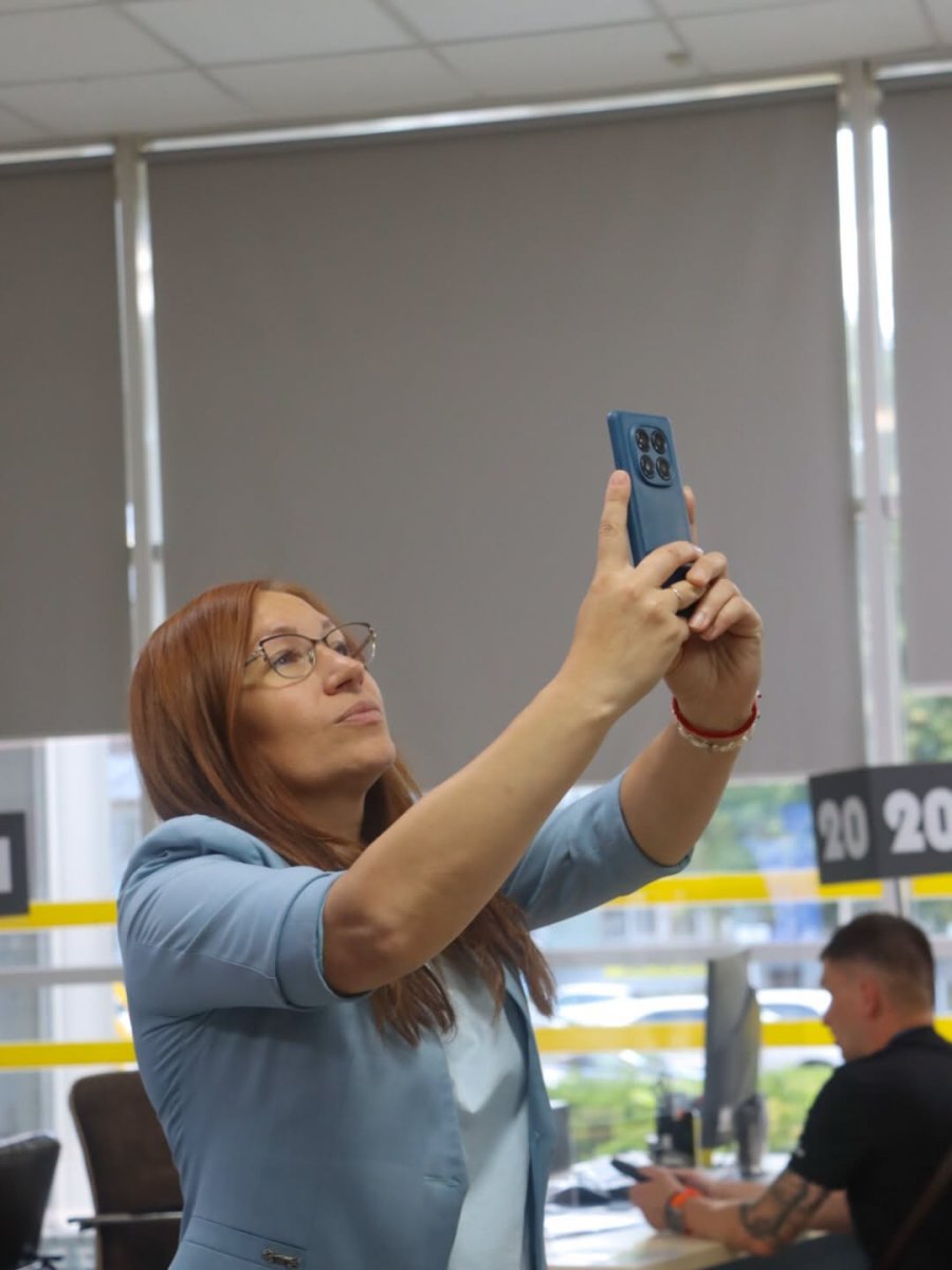 Жінка в окулярах з рудим волоссям фотографує на телефон.