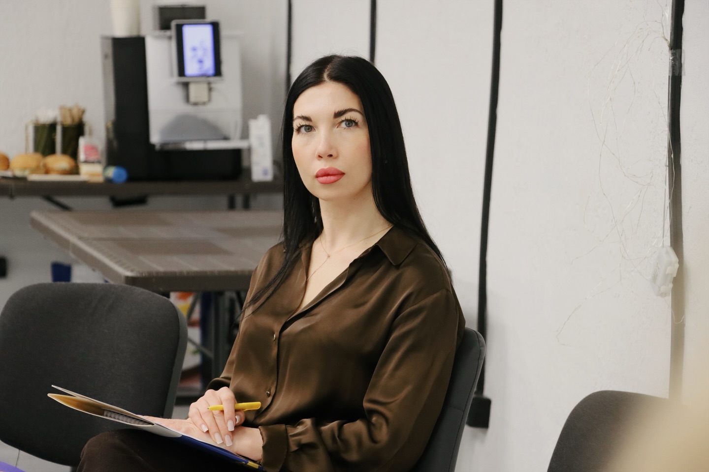 Жінка з довгим чорним волоссям сидить у приміщенні.
