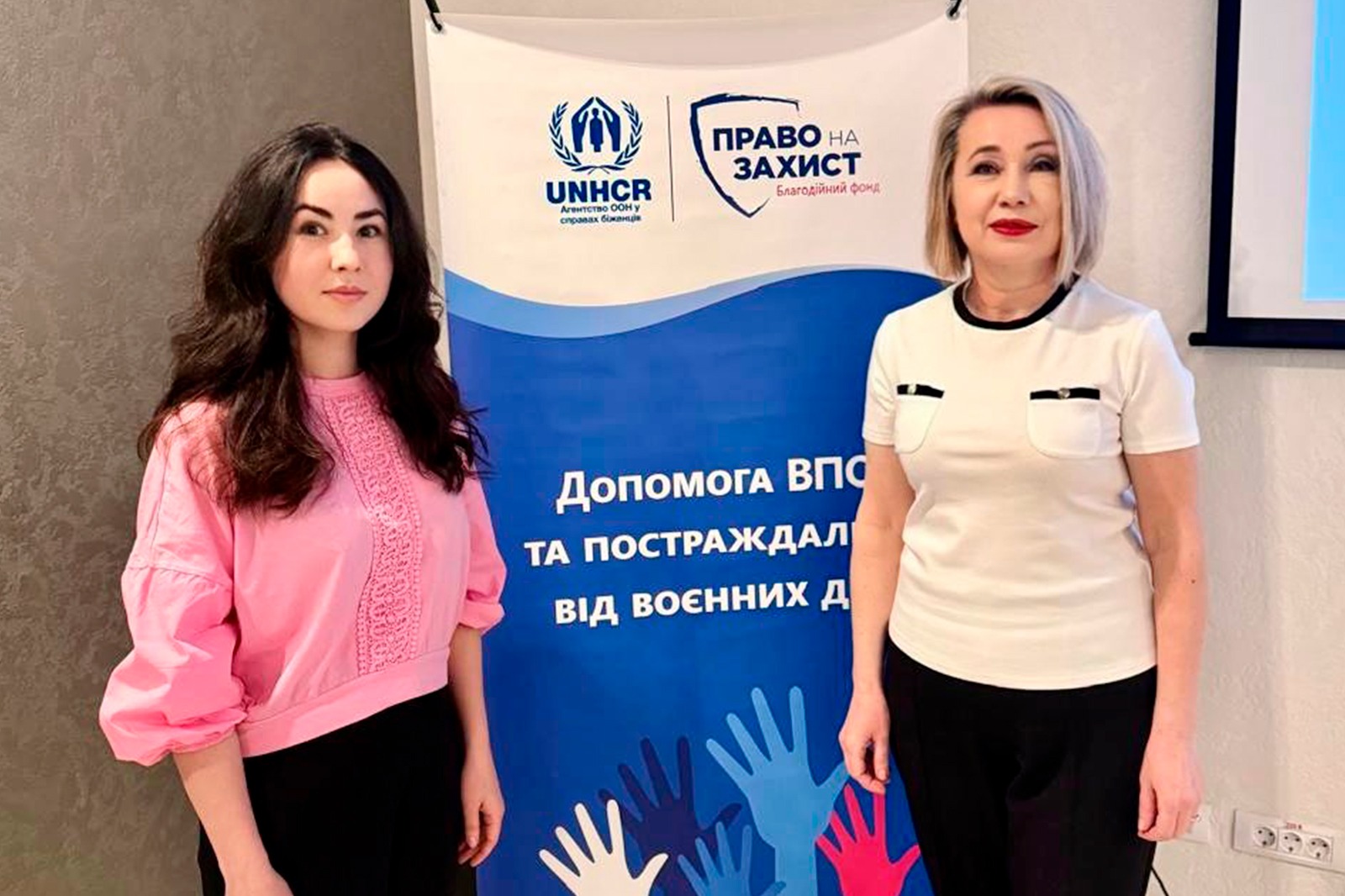 Дві жінки позують на фоні банера.