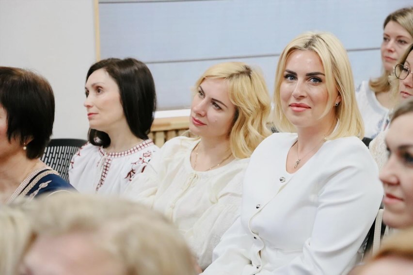 Жінки у білому одязі сидять у залі.