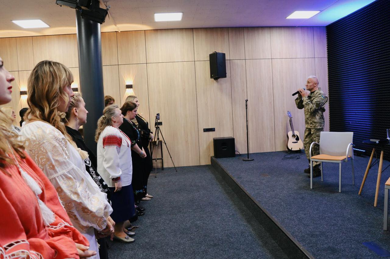 Чоловік у військовій формі тримає мікрофон, жінки стоять перед ним.