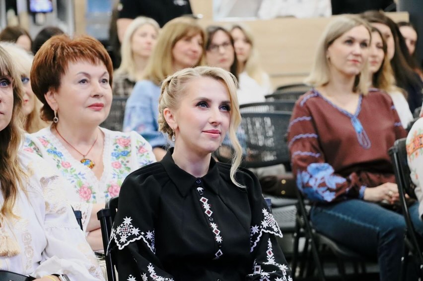 Жінки у вишитих сорочках сидять у залі.