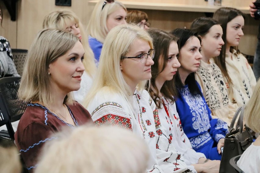 Група жінок у вишиванках сидять у залі.