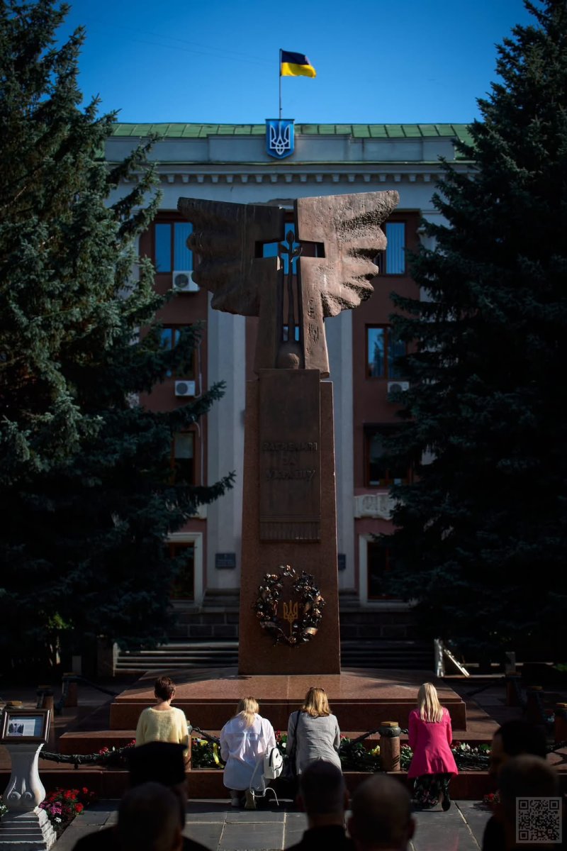 Чотири жінки стоять навколішки перед пам'ятником.