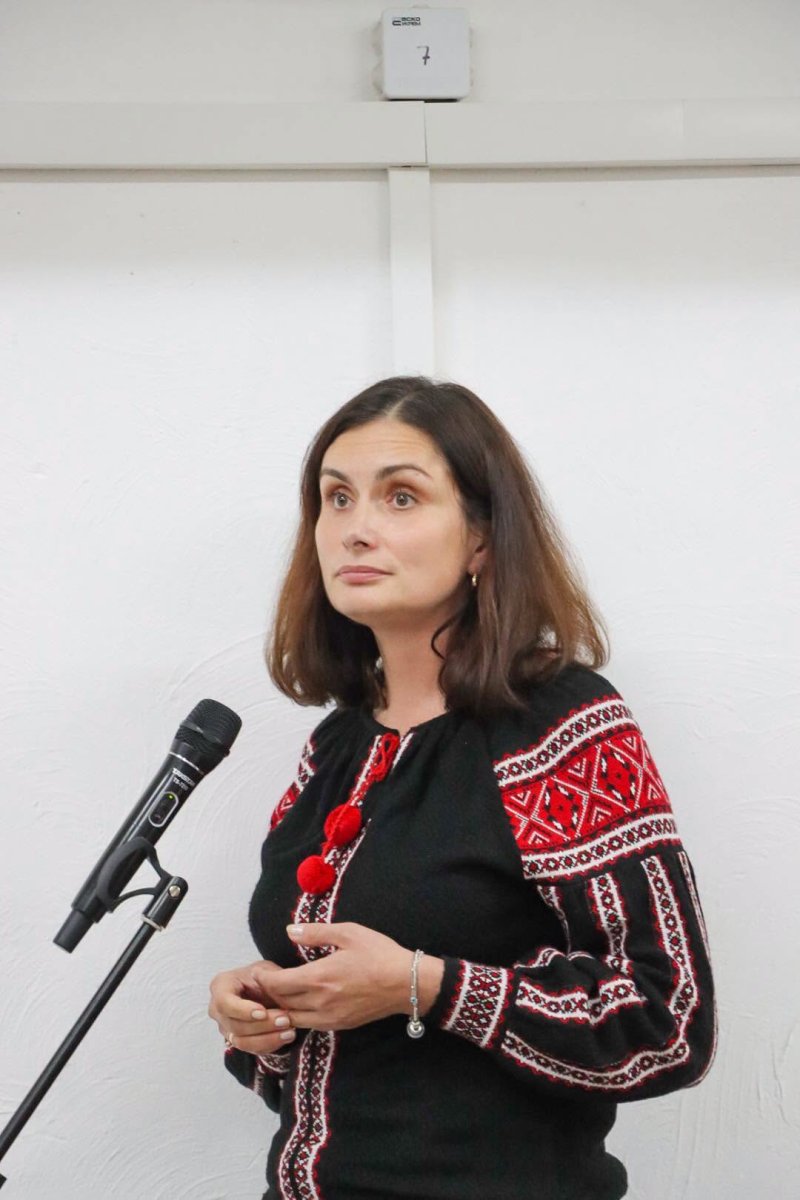 Жінка у вишитій сорочці стоїть біля мікрофону.
