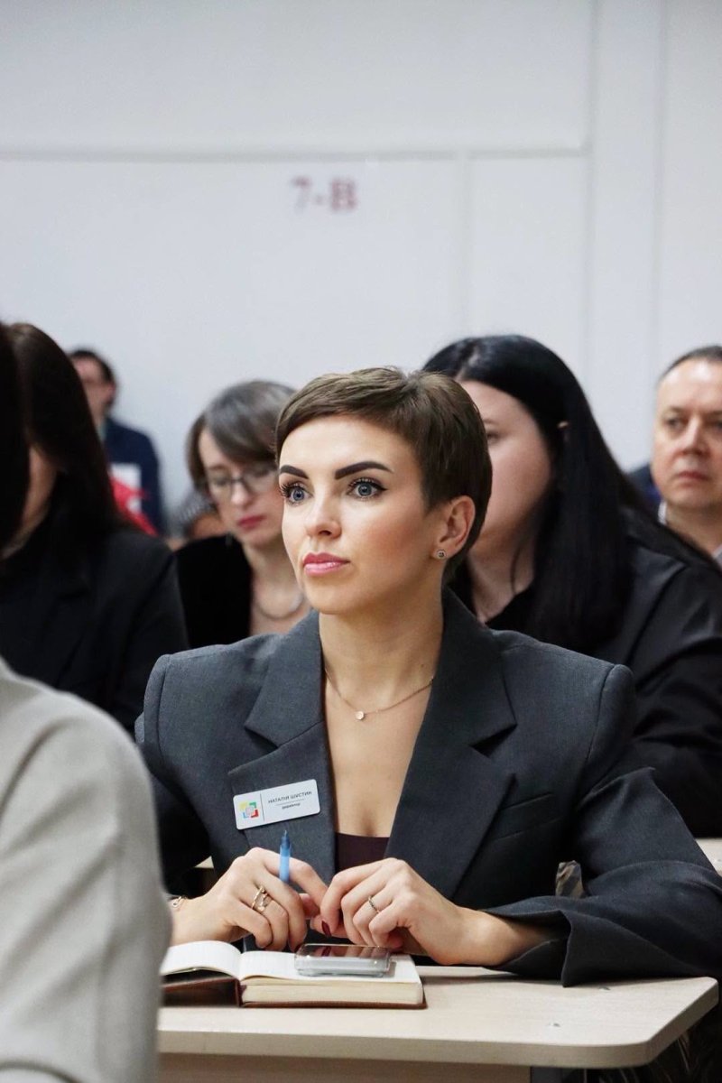Жінка в діловому одязі сидить у приміщенні.