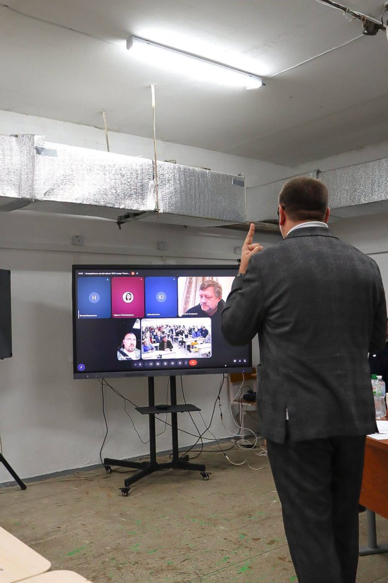 Чоловік стоїть перед телевізором з відеоконференцією.