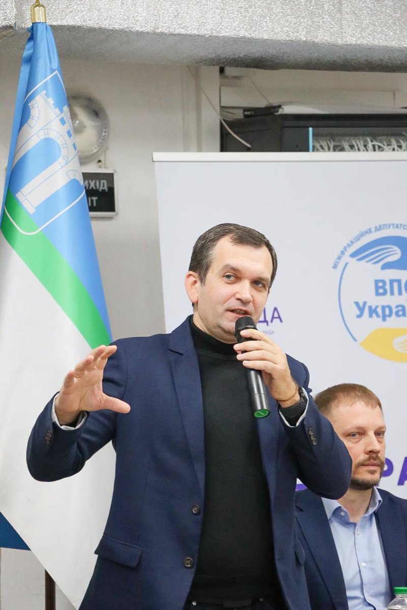 Чоловік у діловому одязі тримає мікрофон у руці.