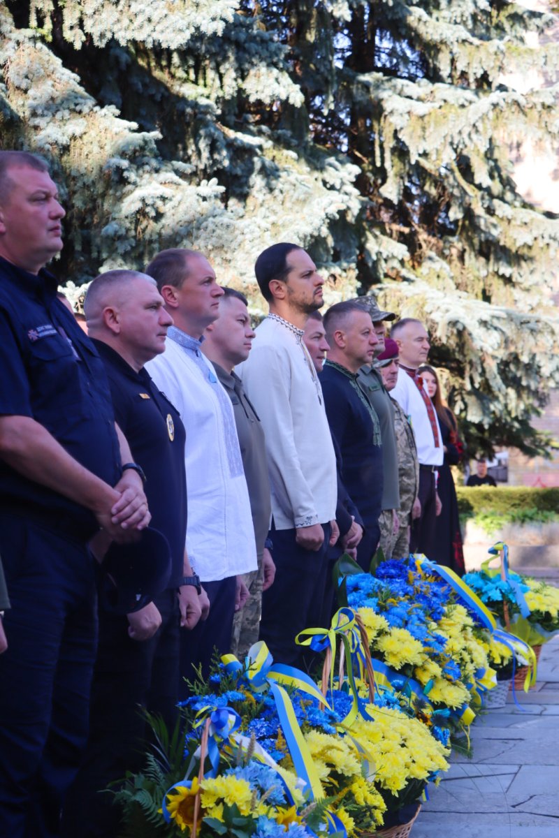 Група чоловіків стоять біля квітів.
