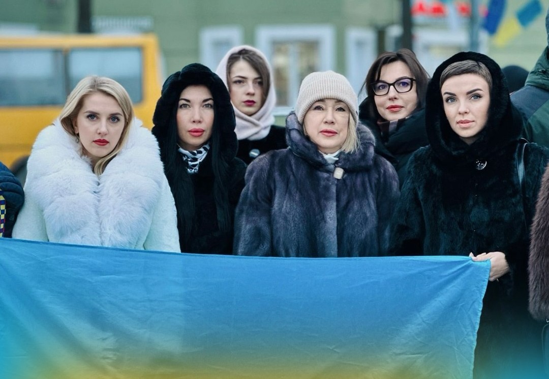 Група жінок перебувають надворі та тримають прапор України у руках.