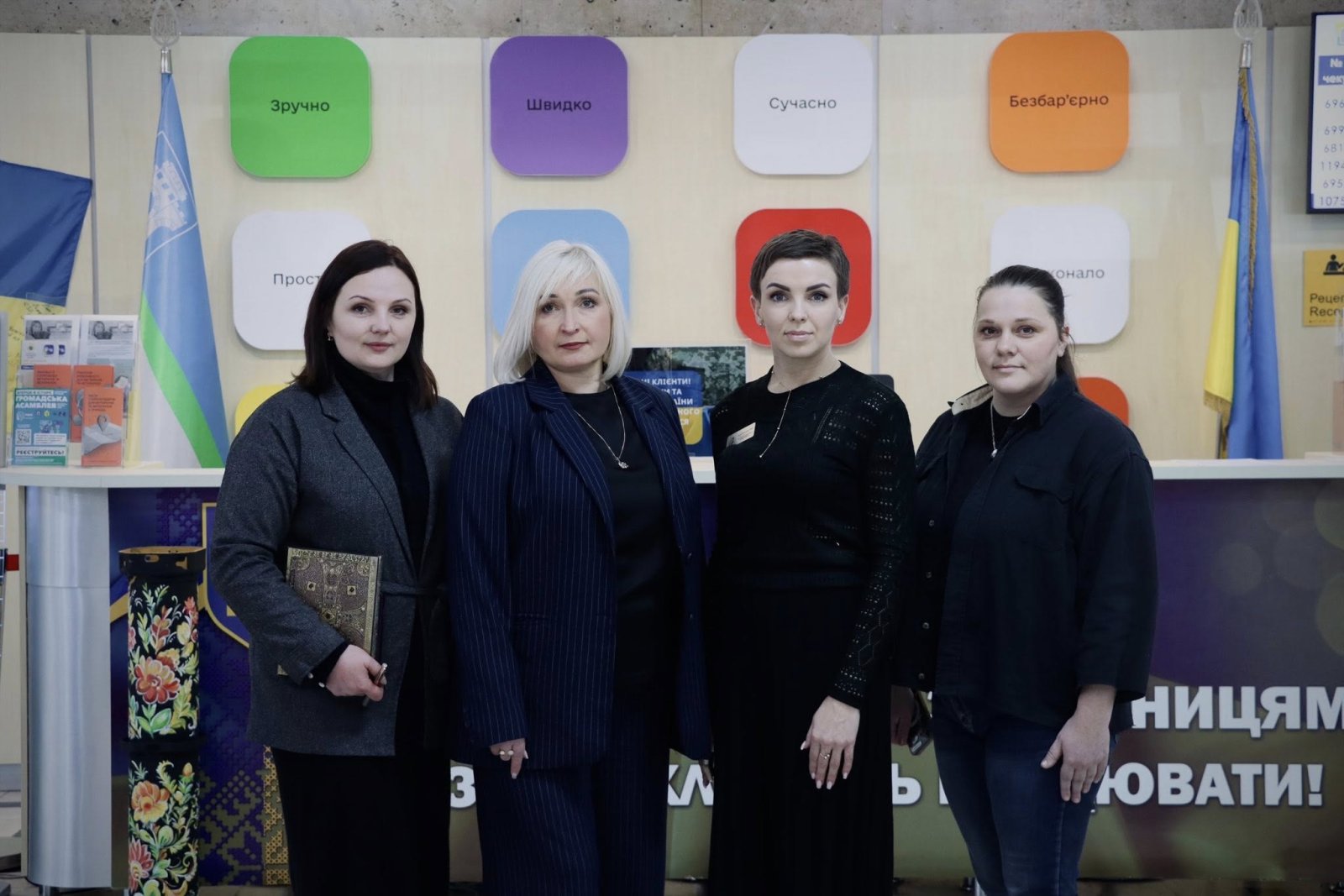 Чотири жінки в темному одязі позують для спільного фото у приміщенні.