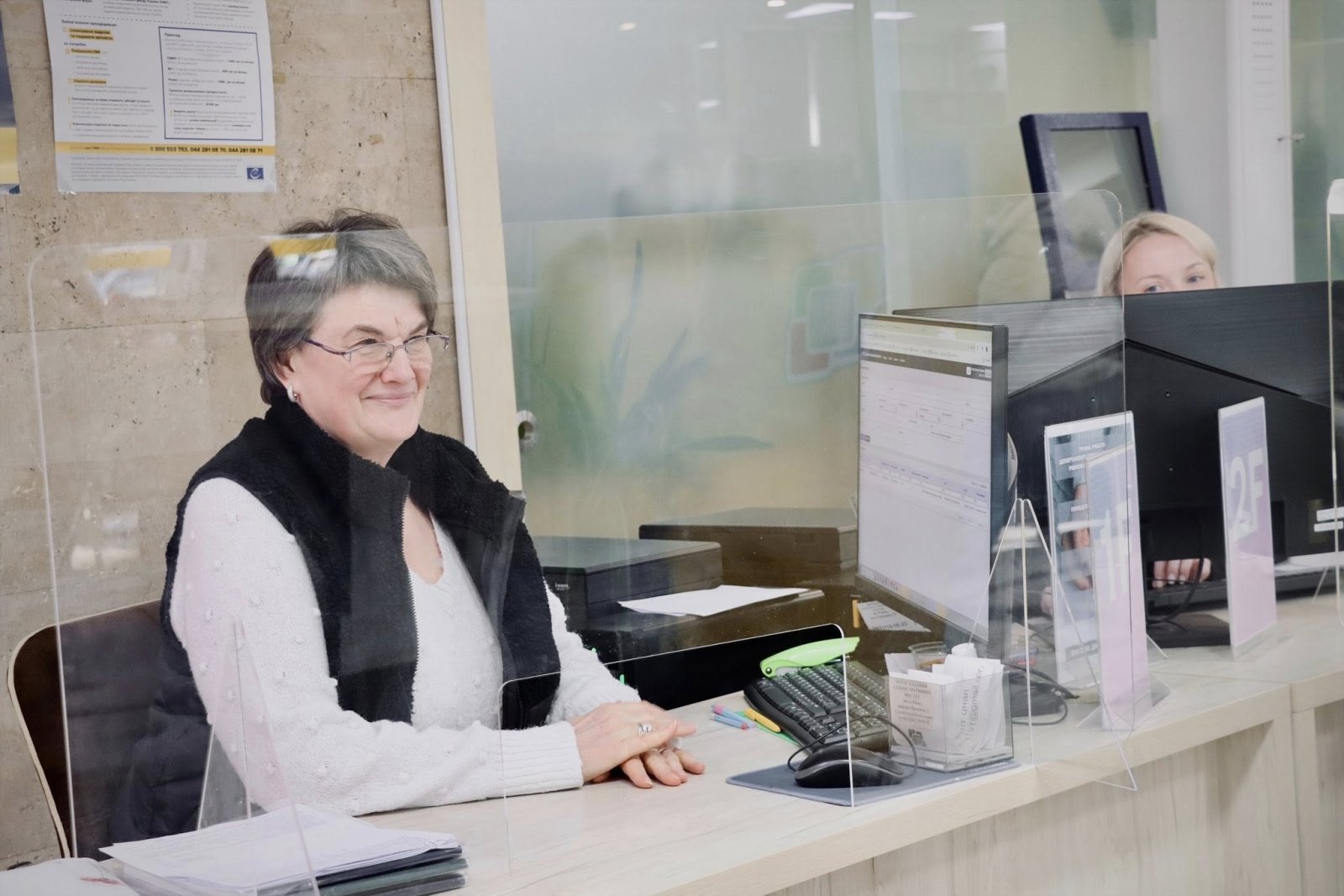 Жінка сидить за столом та посміхається.