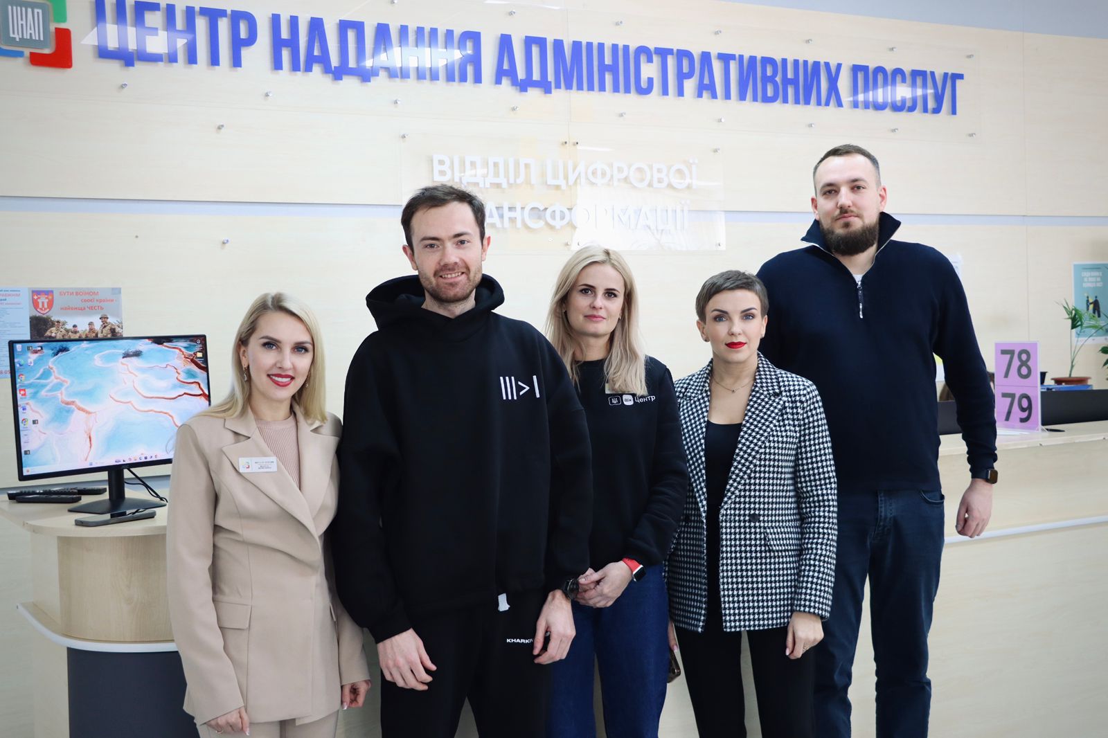 Три жінки та два чоловіка позують для фото у приміщенні.