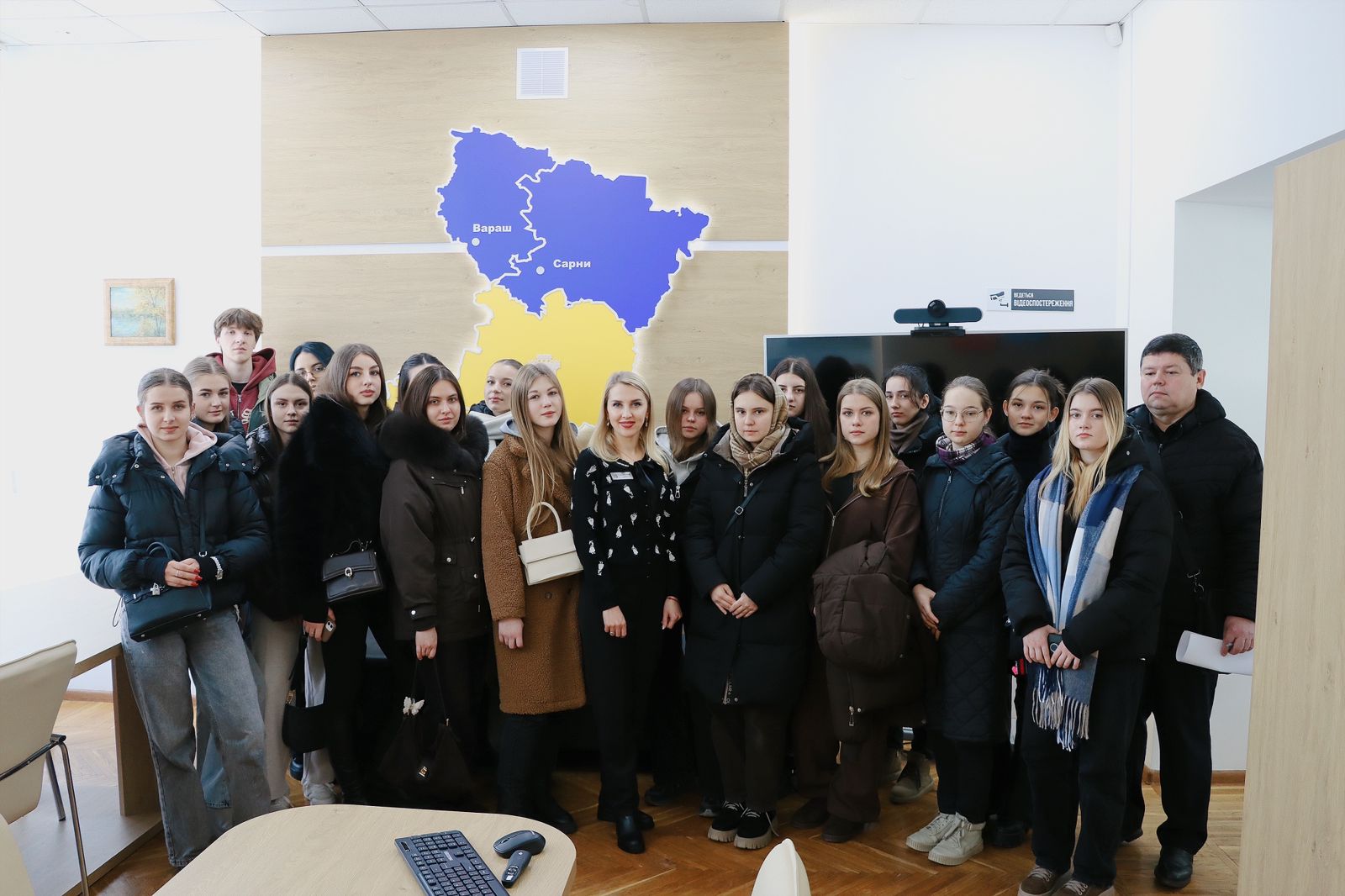 Групове фото у приміщенні, на задньому фоні - карта Рівненщини у синьому та жовтому кольорах.