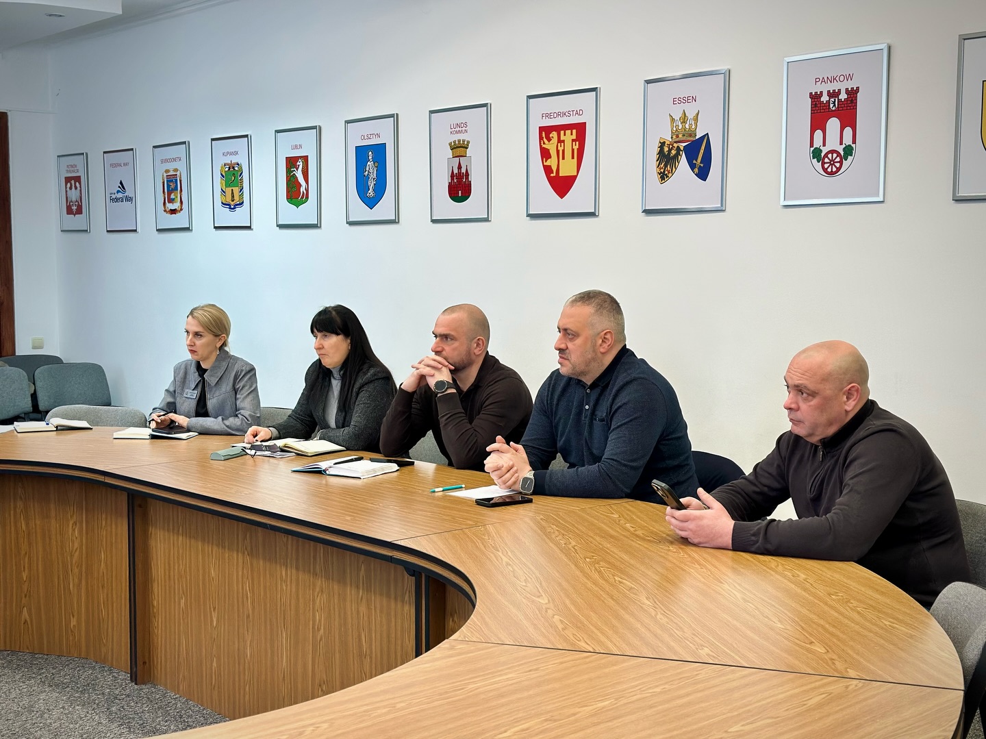 Дві жінки та троє чоловіків сидять за столом, на столі лежать папери