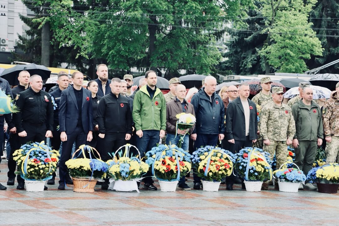 Люди перебувають на вулиці, перед ними стоять корзини з квітами.
