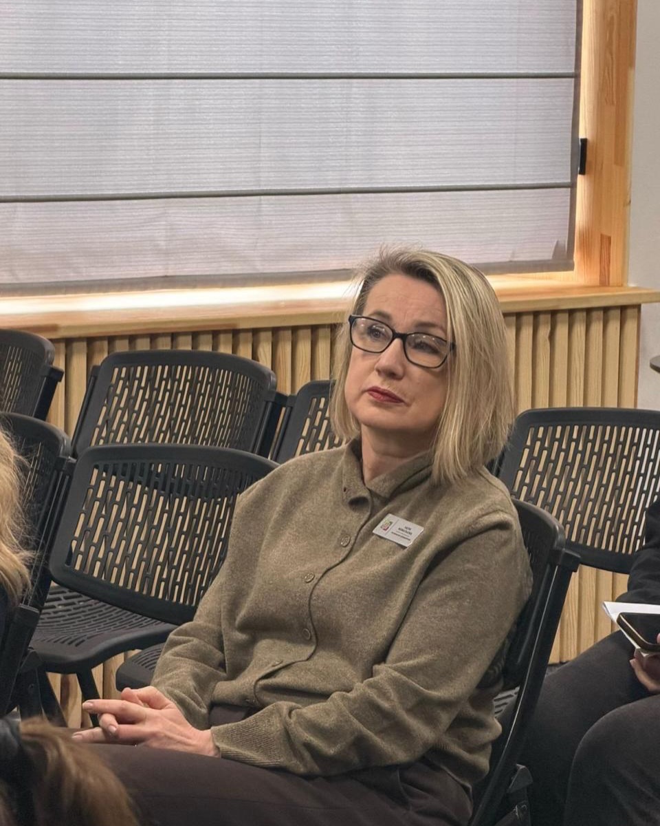 Фото жінки у коричневій кардигані, що сидить на стільці у залі.