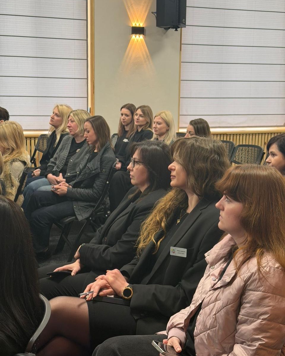 Групове фото жінок, що сидять на стільцях у залі.