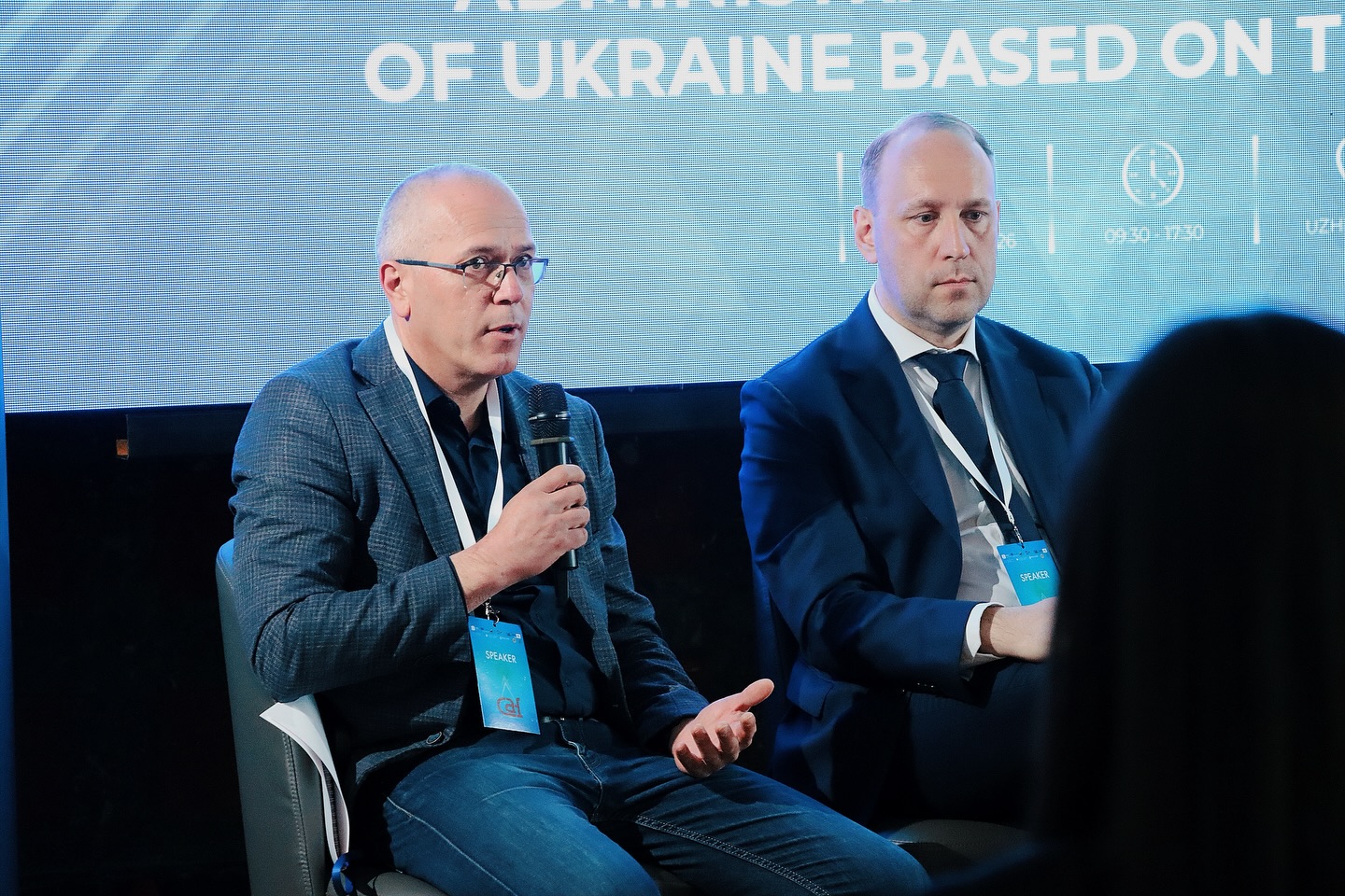 Чоловік тримає мікрофон у руках, біля нього сидить ще один чоловік.