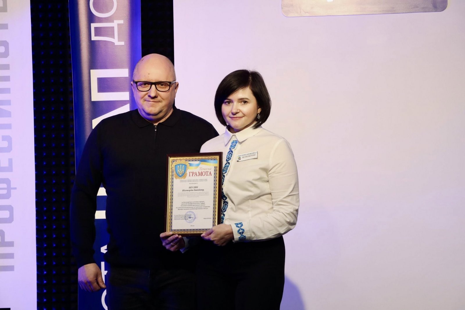 Чоловік в окулярах стоїть біля жінки з нагородою в руках