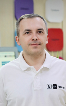 Чоловік із темно-русявим волоссям і світлою шкірою у білій футболці. У приміщенні. Вираз спокійний.